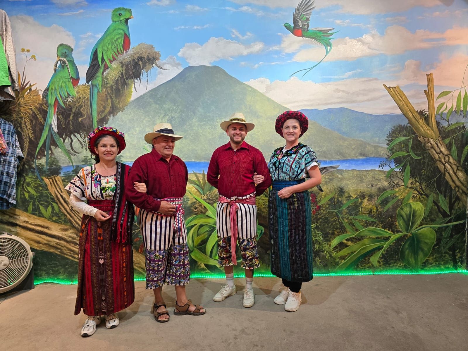 Grupo de personas en un acantilado, con una bandera, sonriendo. Montaña y cielo al fondo.