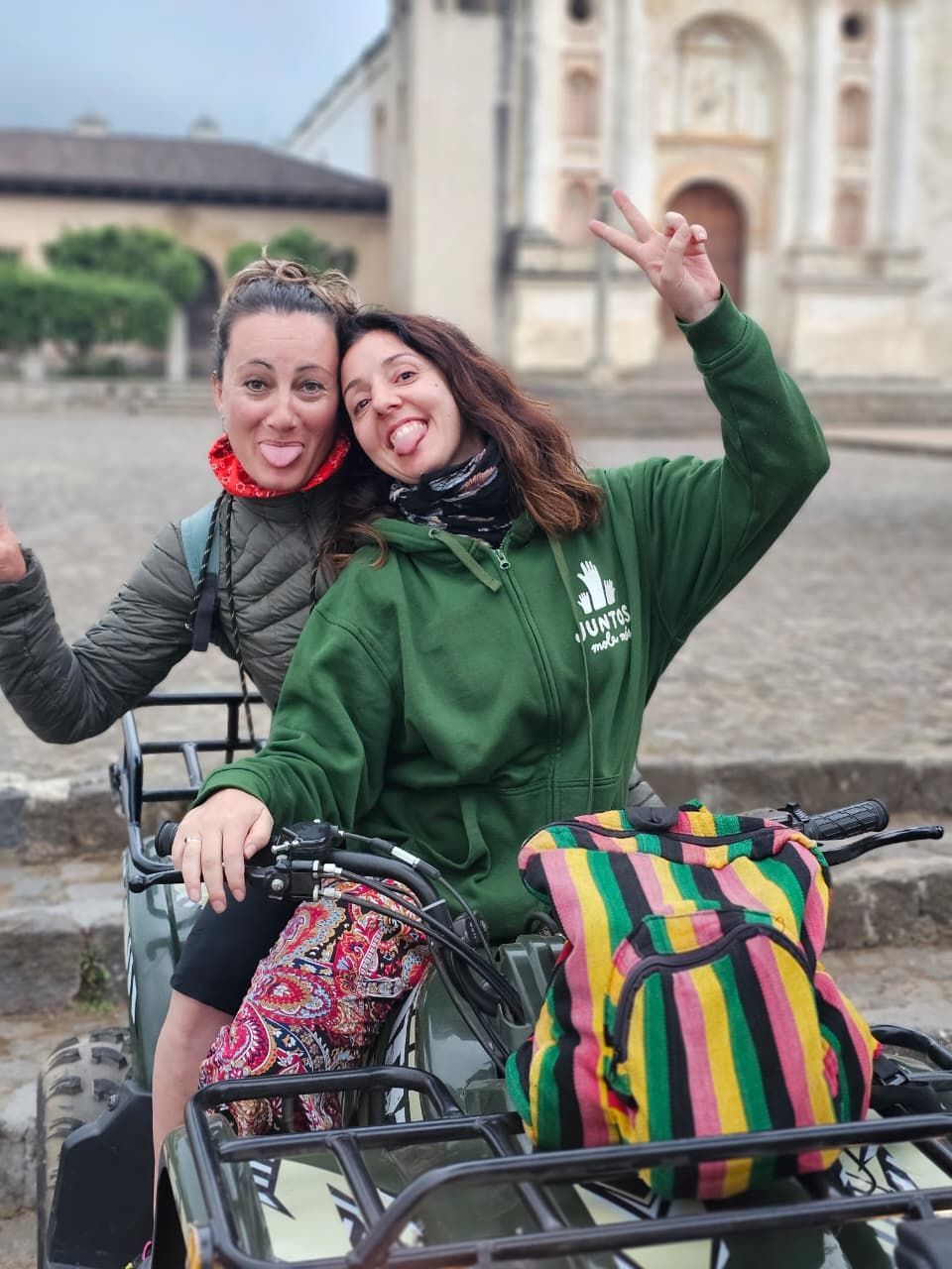 Grupo de personas en un acantilado, con una bandera, sonriendo. Montaña y cielo al fondo.