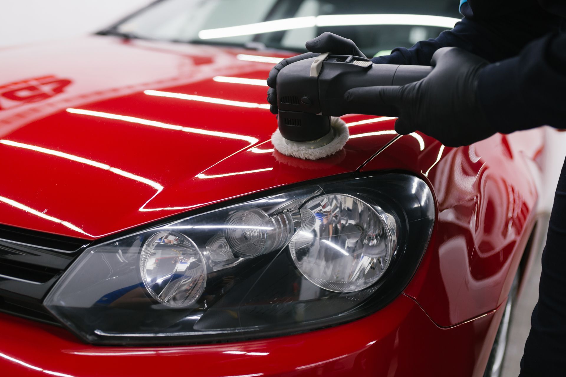 A person polishing a red car hood with a machine polisher