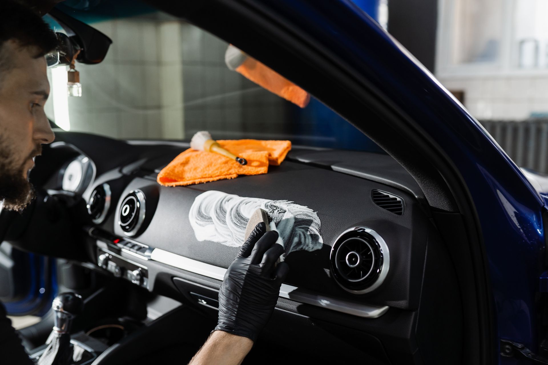 Man in black gloves cleaning a car dashboard with a cloth