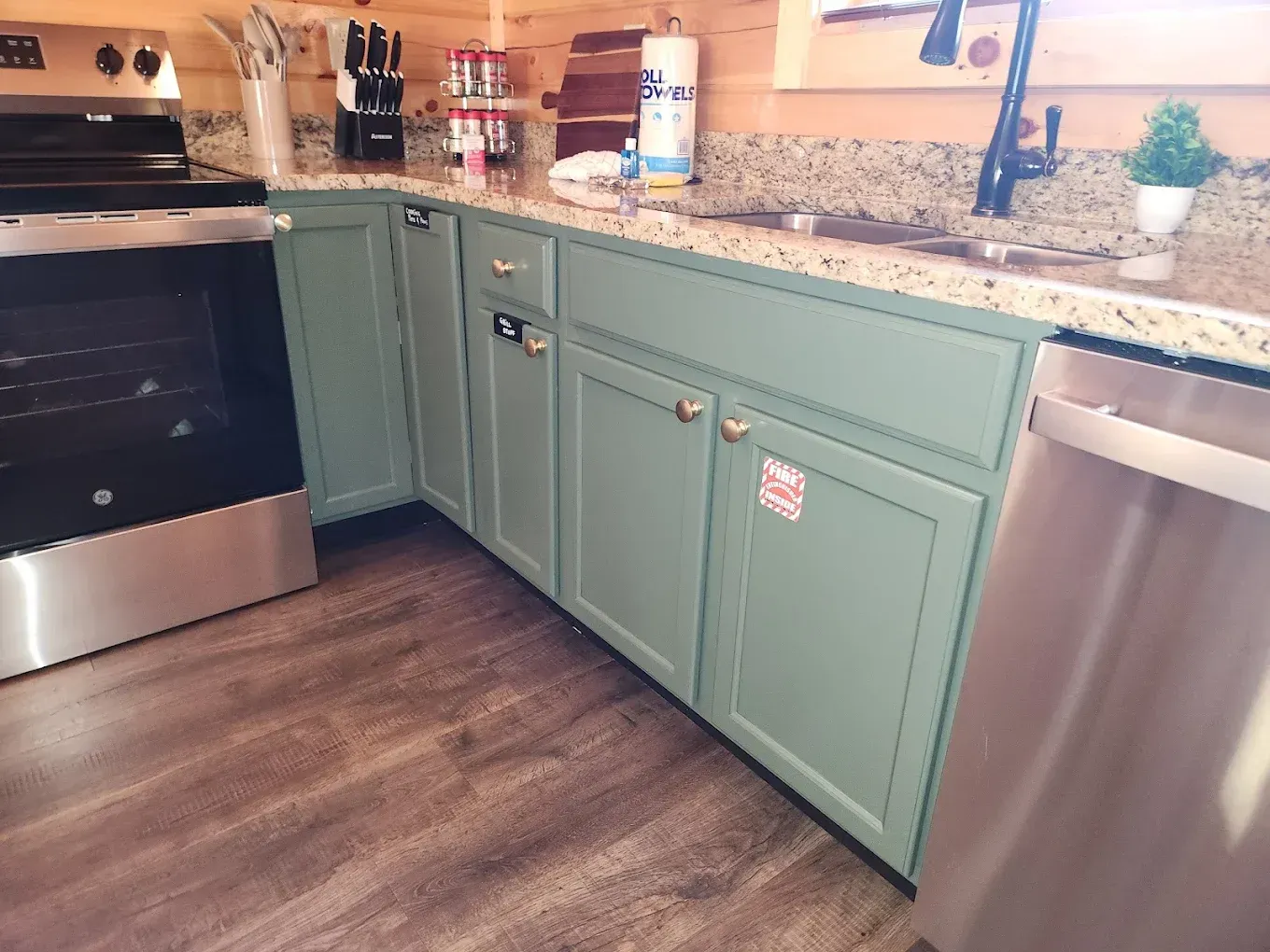 Green kitchen cabinets with gold hardware, granite countertop, and stainless steel appliances.