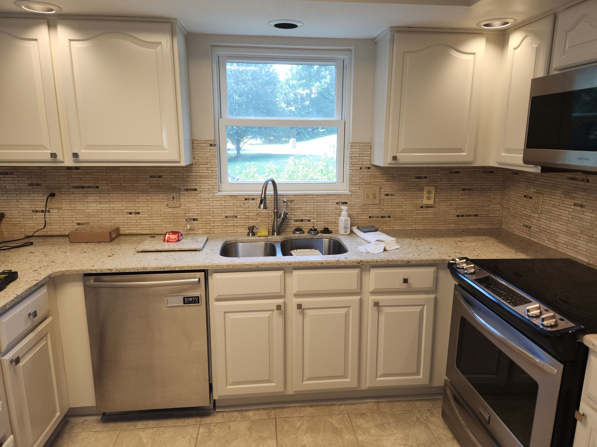 White kitchen with stainless steel appliances, a sink, and window above.