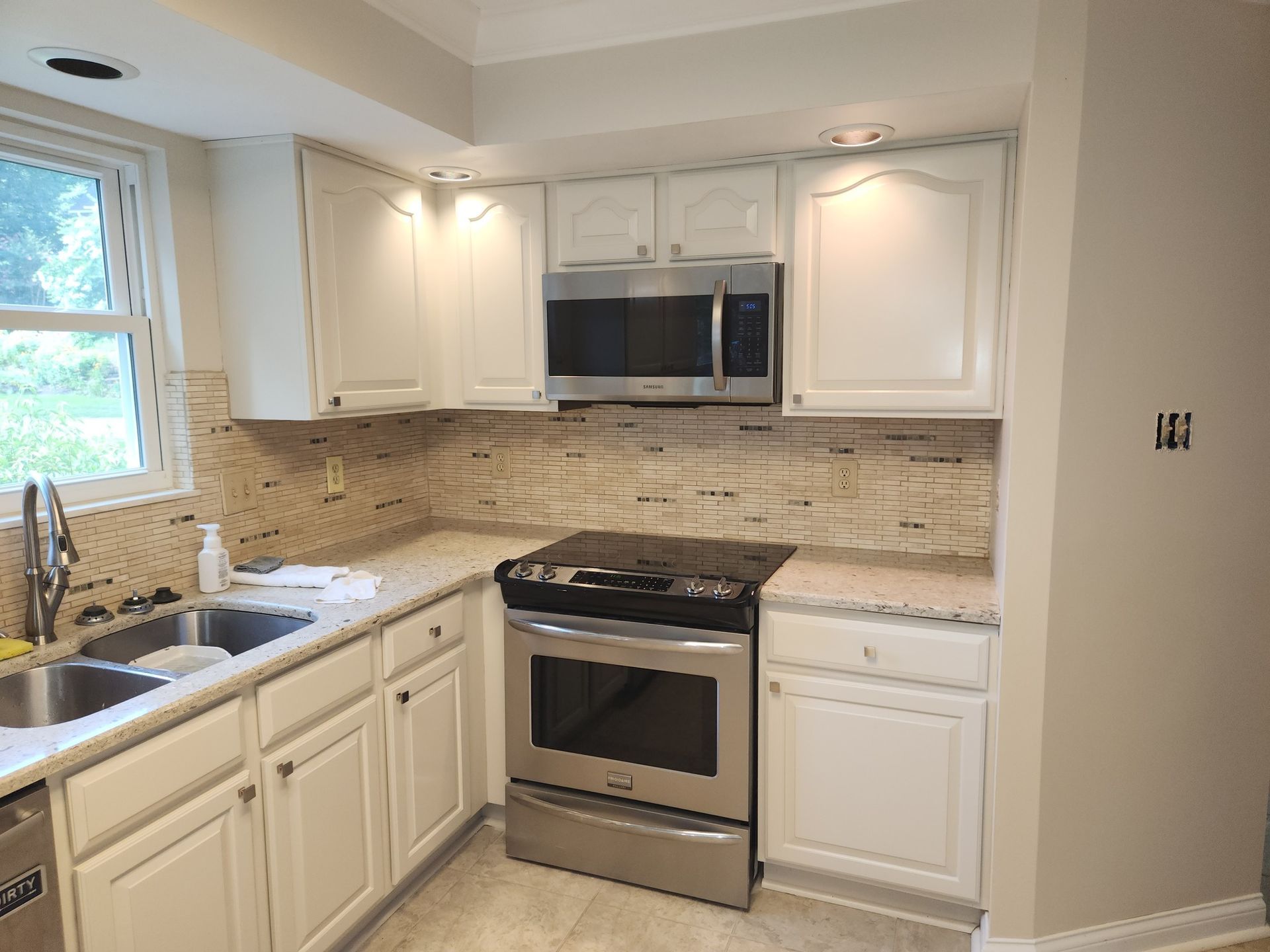 White kitchen cabinets with stainless steel appliances, stone backsplash and countertop.