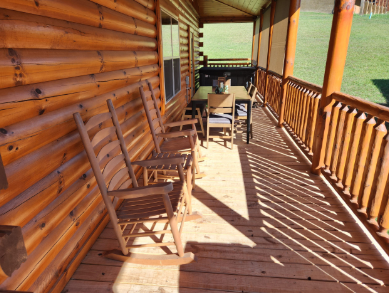 Wooden porch with rocking chairs and a table, overlooking a green yard.