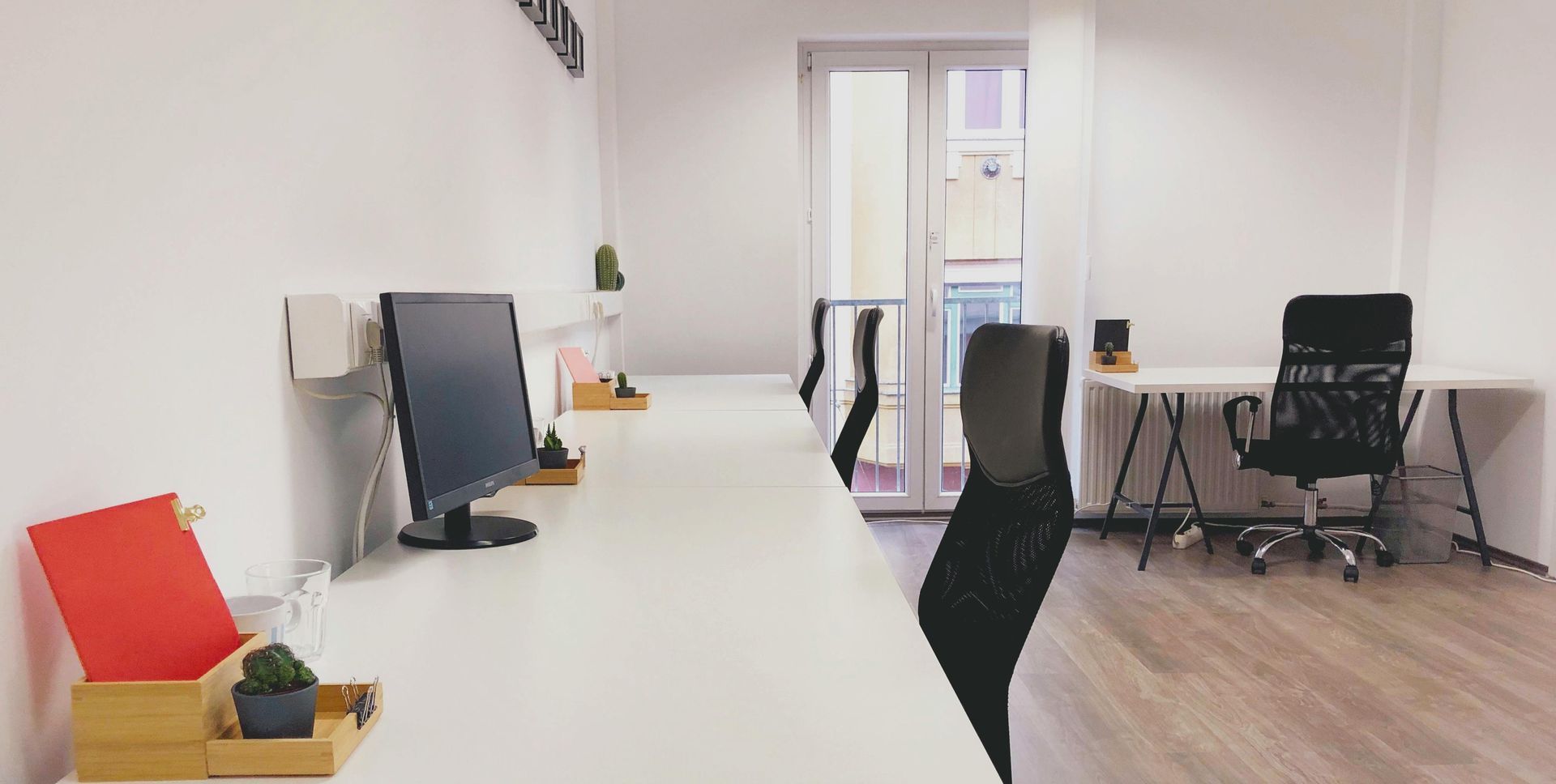 Bright office space with white desks, black chairs, and a view of a window.