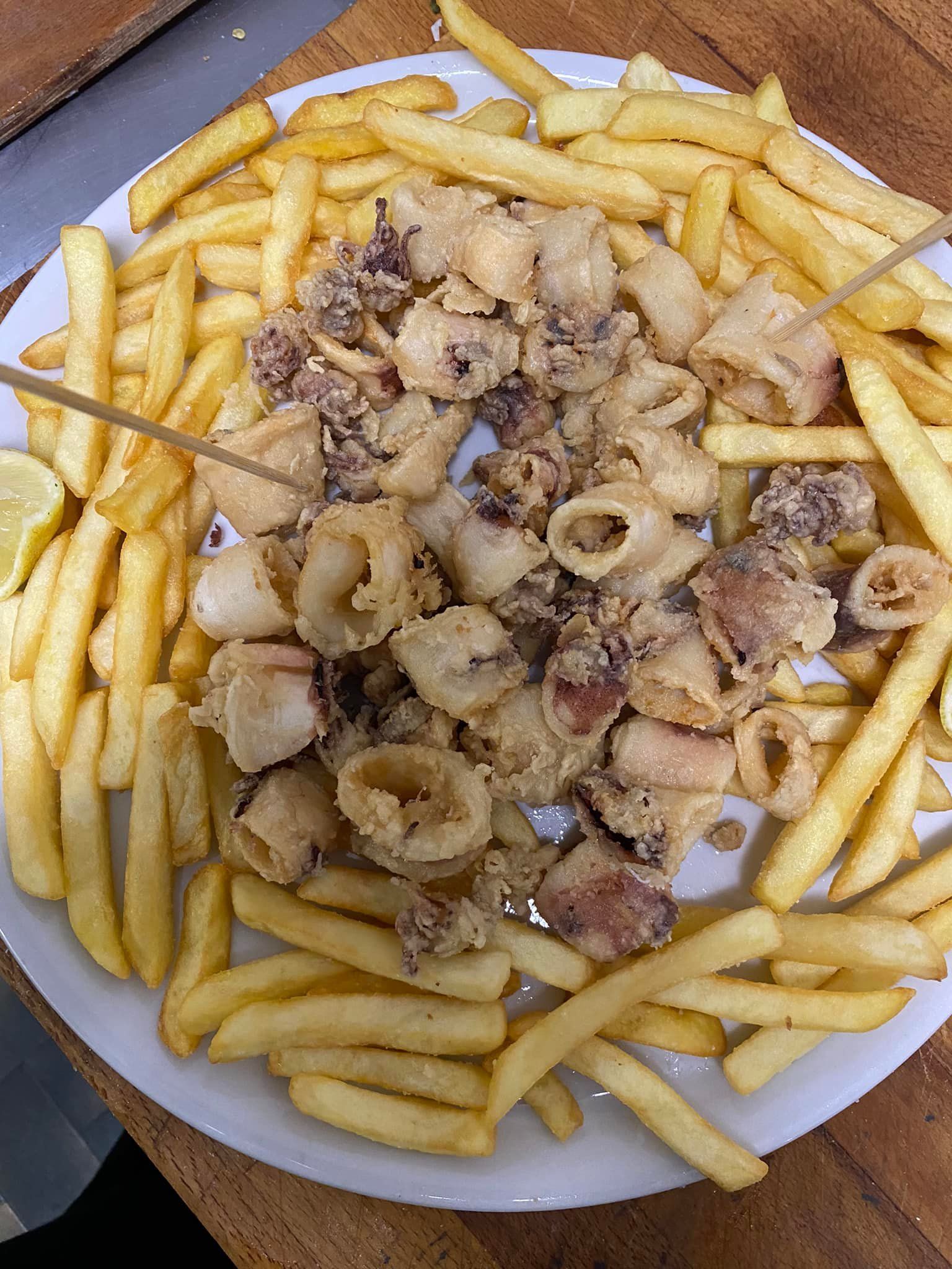 Un piatto di calamari fritti e patatine fritte su un tavolo di legno.