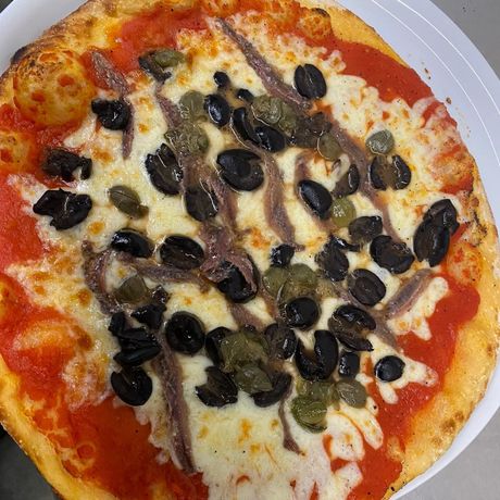 Una pizza con salsa di pomodoro, formaggio, olive e capperi su un piatto bianco.