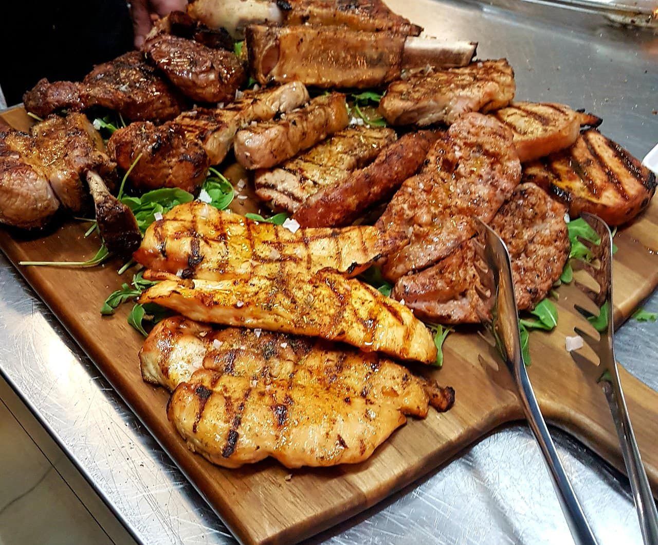 Un tagliere di legno riempito con una varietà di carni alla griglia