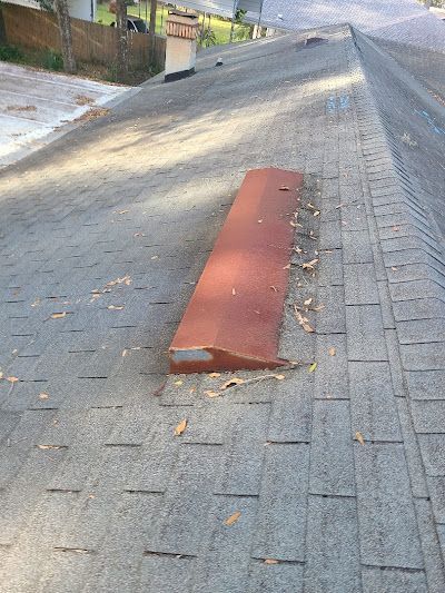 A weathered, reddish-brown rectangular roof vent sits on a gray shingled roof under bright daylight.