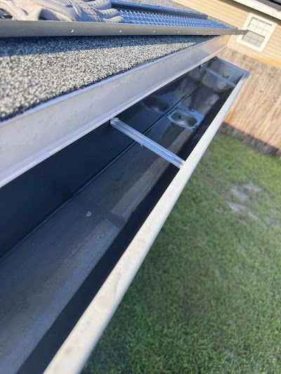 A low-angle view of a clean, empty metal rain gutter attached to a roof edge with a mesh gutter guard installed above it.