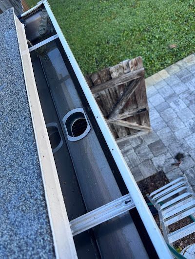 A high-angle view of a clean, dark-colored rain gutter on a roof edge, featuring a circular downspout hole.