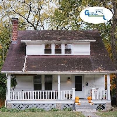 A white, two-story house with a front porch, a gabled roof, and orange pumpkins sitting on the porch steps.