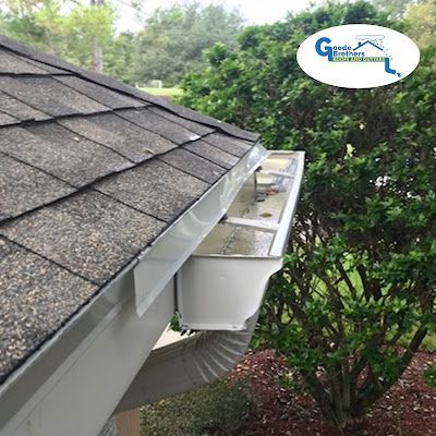 A side-view of a clean white gutter system installed on a residential roof, with a downspout and a company logo above.