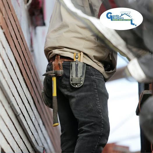 A construction worker wearing a tool belt with a hammer, standing beside a building with brown siding.