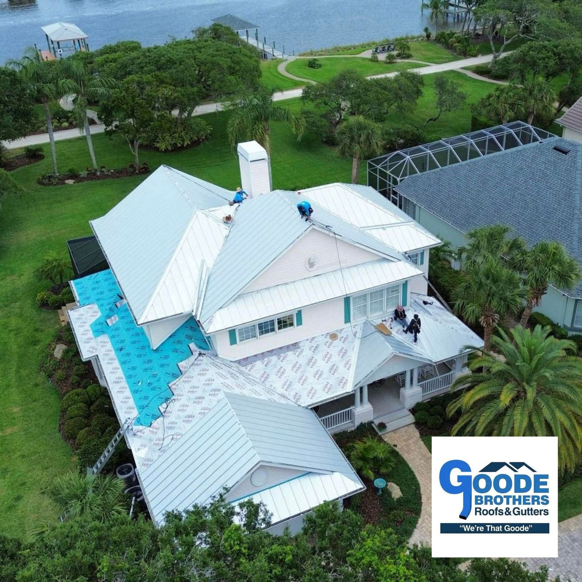 Aerial view of a house during a metal roof installation, with construction workers on the roof and a company logo overlay.