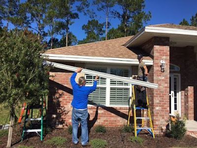 Two people work together to install a gutter along the roofline of a brick house.