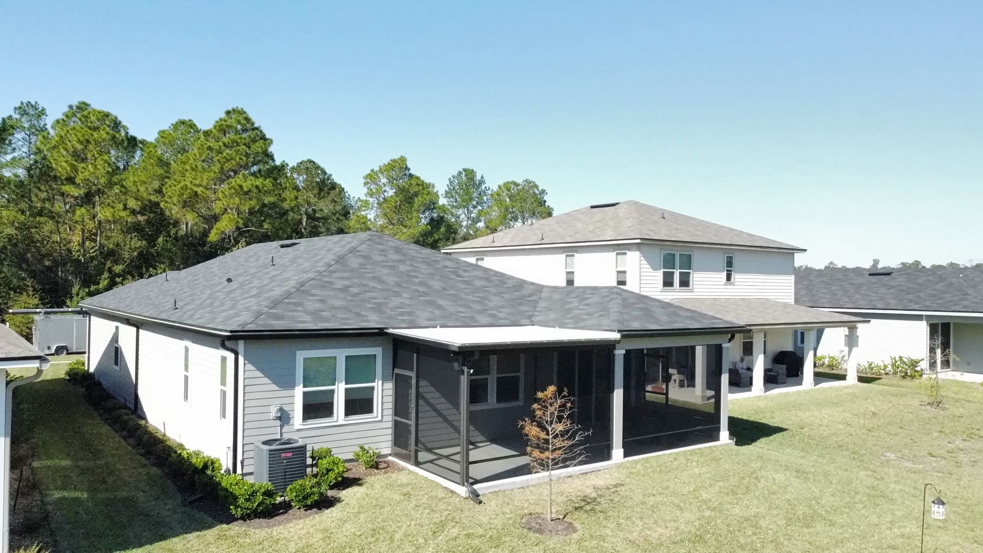 An aerial view of a single-story gray house with a screened-in back porch next to a two-story white house on a sunny day.