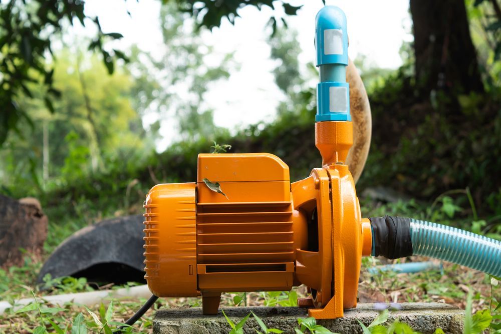 Orange Water Pump Connected to a Blue Hose Outdoors on Grass — Taree Water Works in Taree, NSW