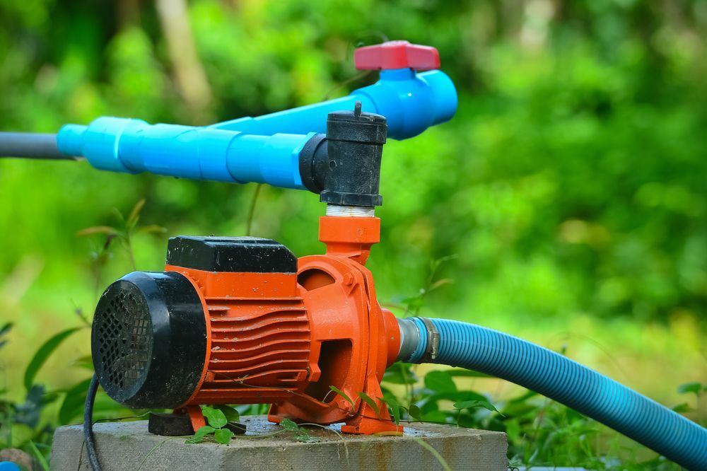 Orange Water Pump Connected to Blue Pipes With Red Valves Outdoors — Taree Water Works in Taree, NSW