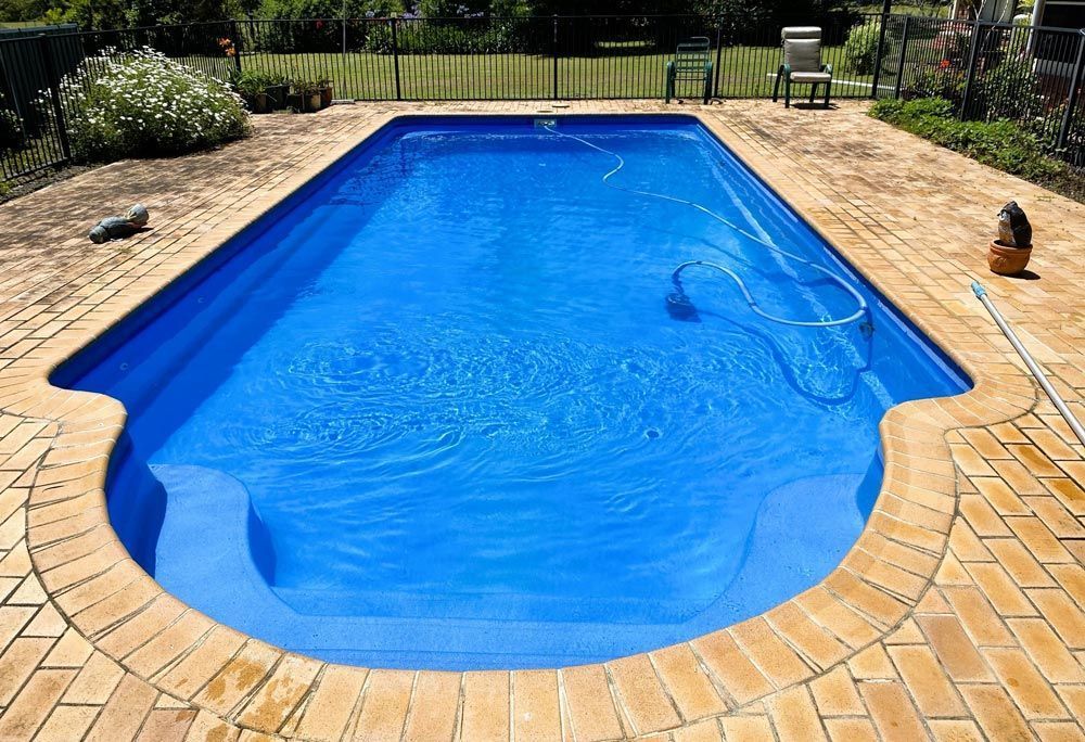 Blue Backyard Swimming Pool with Tan Brick Deck and Hose on The Right Side — Taree Water Works in Taree, NSW