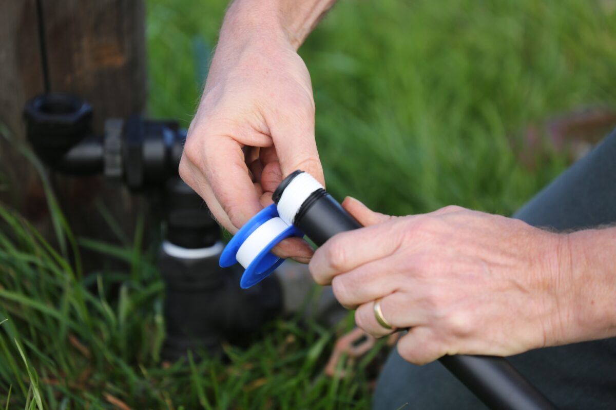 Hands Adjusting a Blue-and-white Connector on a Black Pipe in Grass Outdoors — Taree Water Works in Taree, NSW