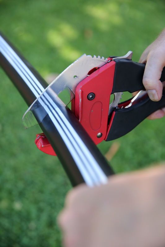 Hands Using a Red-and-black Hand Tool to Cut a Black-and-white Striped Strap — Taree Water Works in Taree, NSW