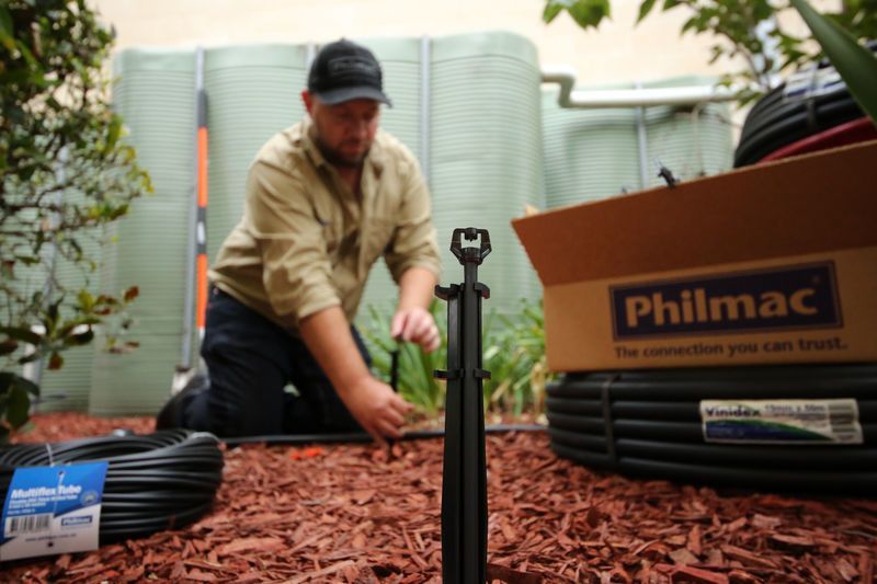 Worker Installing Black Irrigation Tubing in a Garden Beside Philmac Boxes — Taree Water Works in Taree, NSW