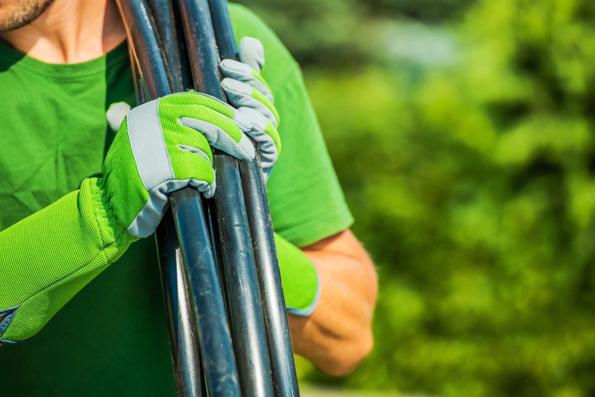Person in Green Shirt Holding Folded Black Metal Poles With Gloved Hands Outdoors — Taree Water Works in Taree, NSW
