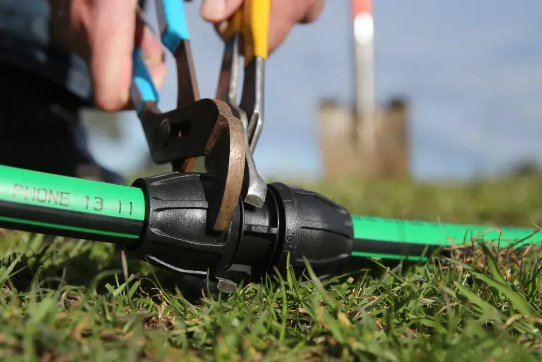 Hands Using Pliers to Repair a Green Garden Hose on Grass — Taree Water Works in Taree, NSW
