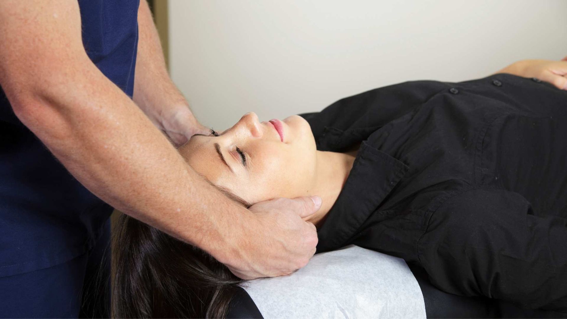 Person receiving a head massage lying down on a massage table. Hands of person massaging head are visible.