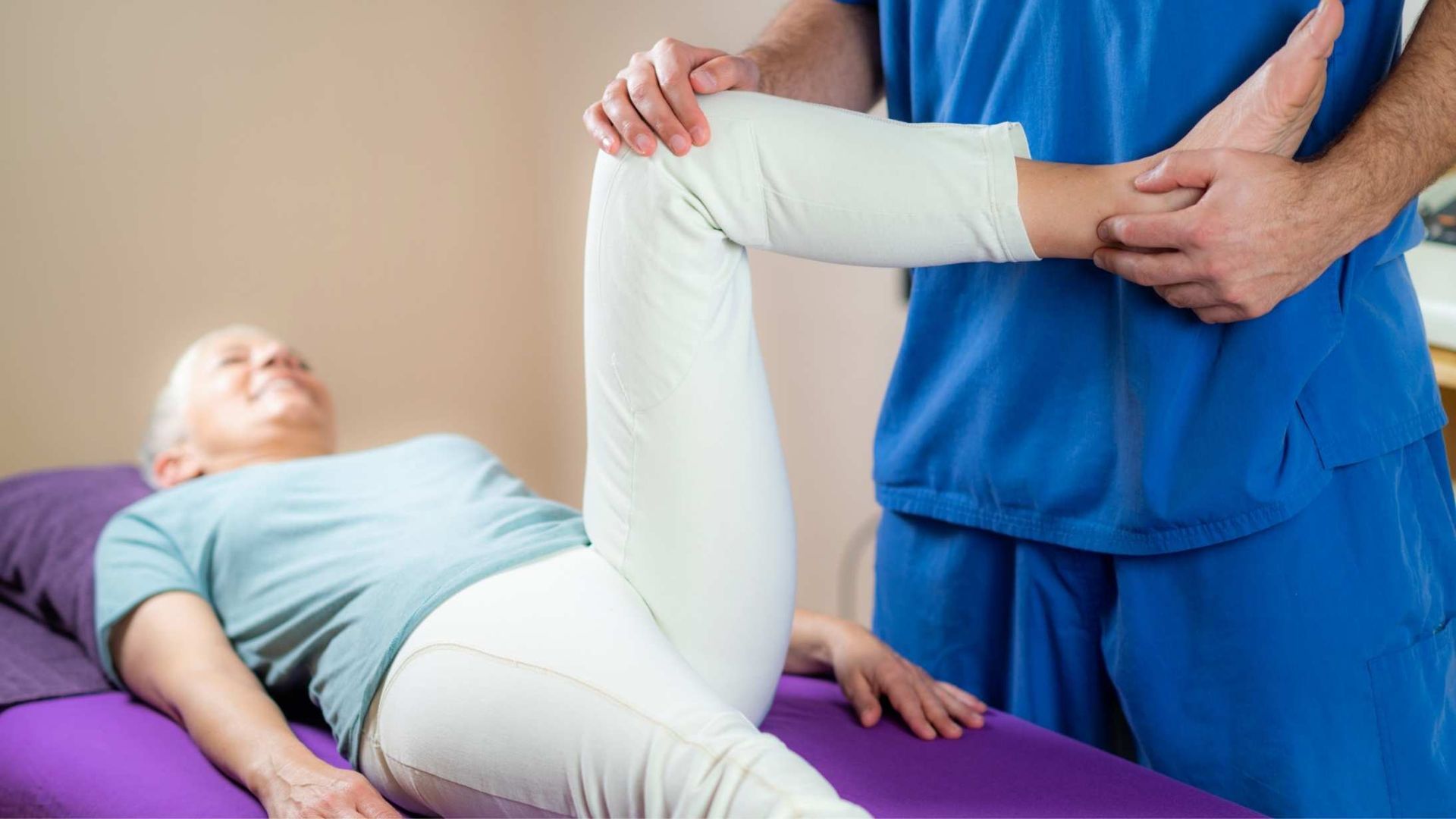 Therapist stretching patient's leg on massage table. Patient smiling.
