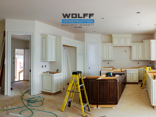 Kitchen under construction with white cabinets, brown island, and yellow ladder.