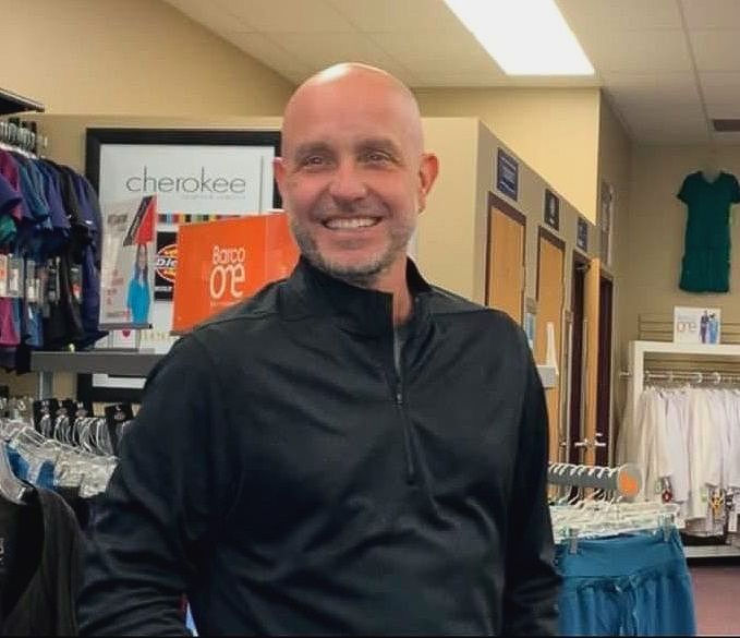 Doug James, a bald man in a black jacket, is smiling in his medical uniform store