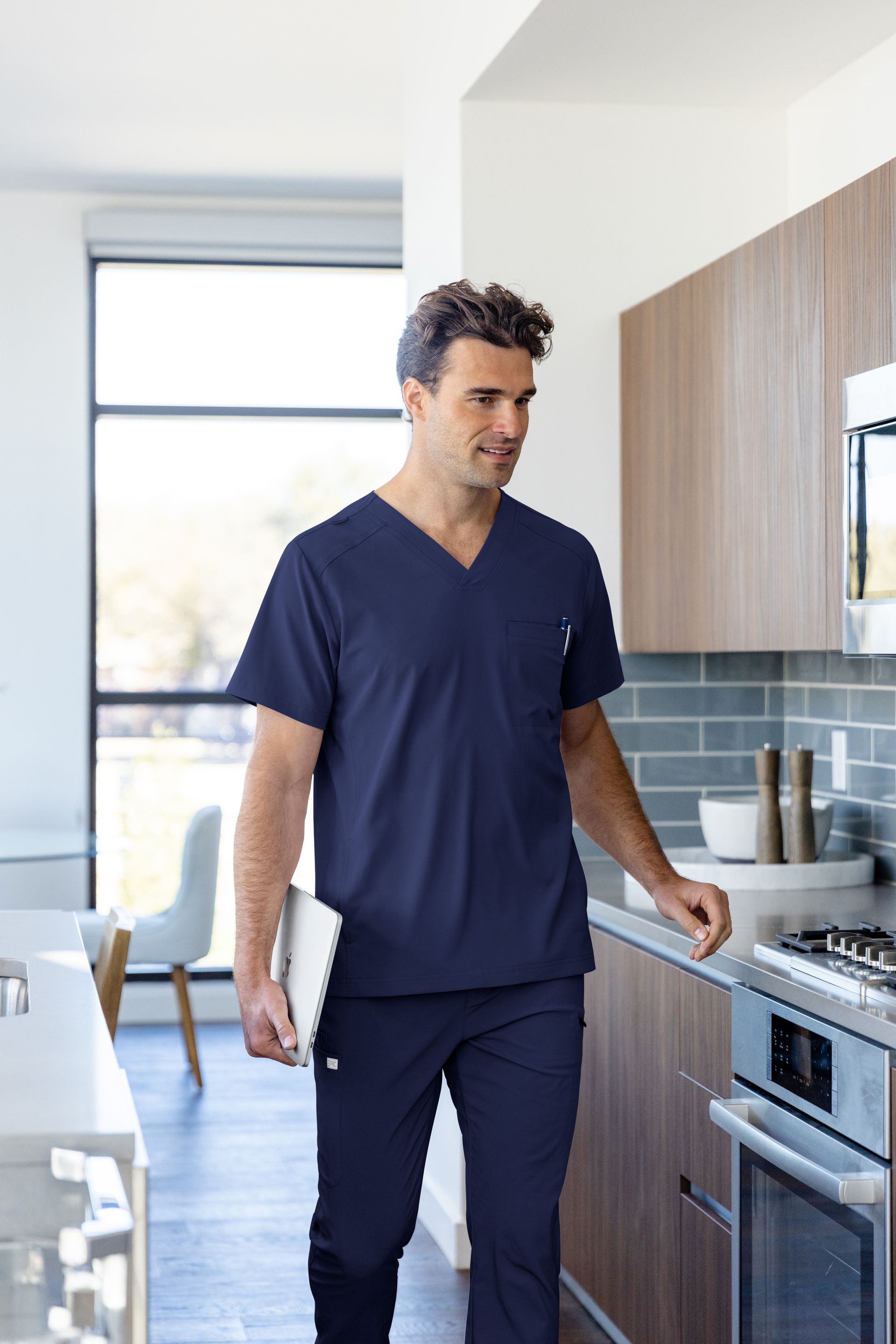 A man in a blue scrub top and pants is walking in a kitchen.