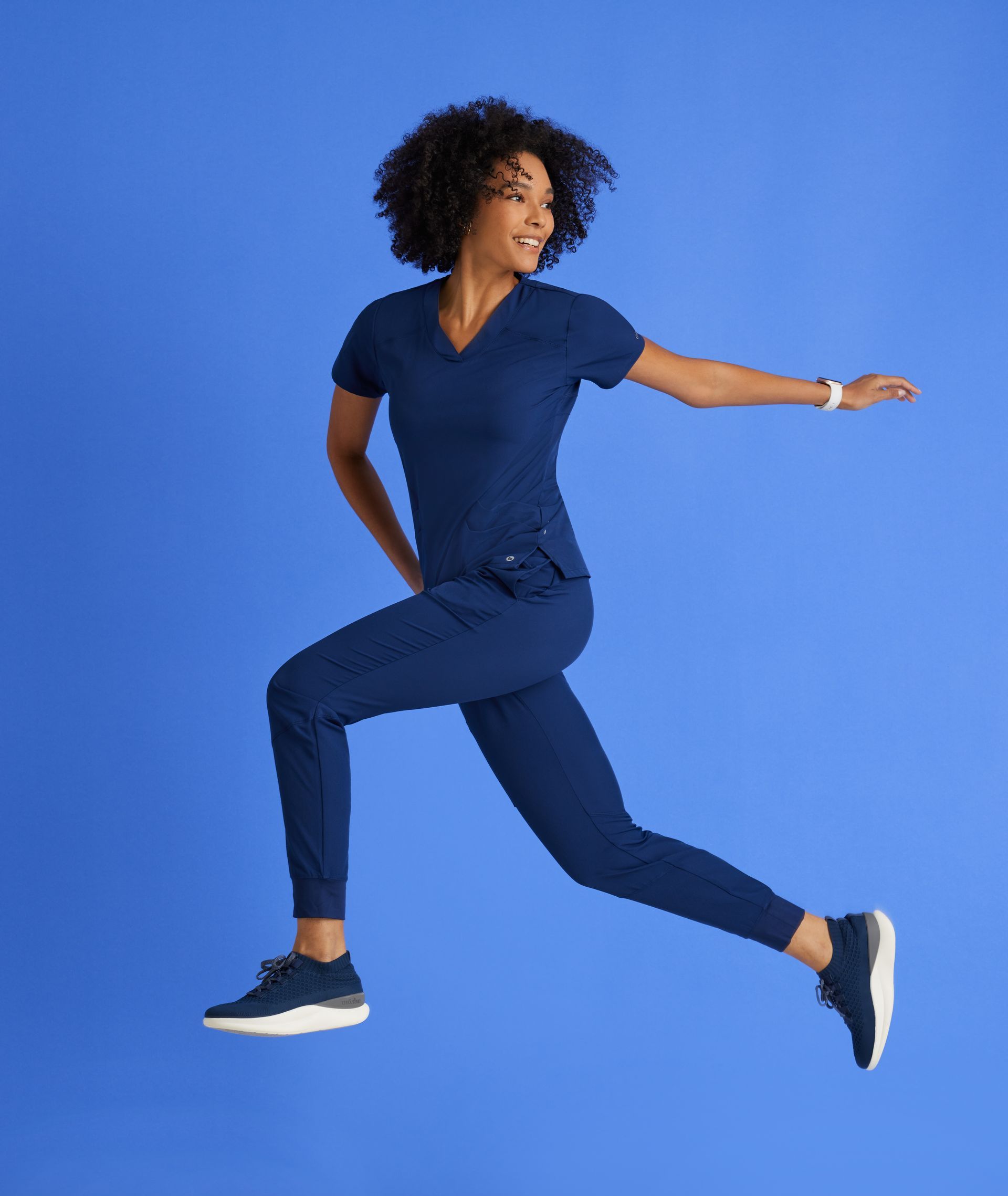 A woman in a blue scrub suit is jumping in the air.
