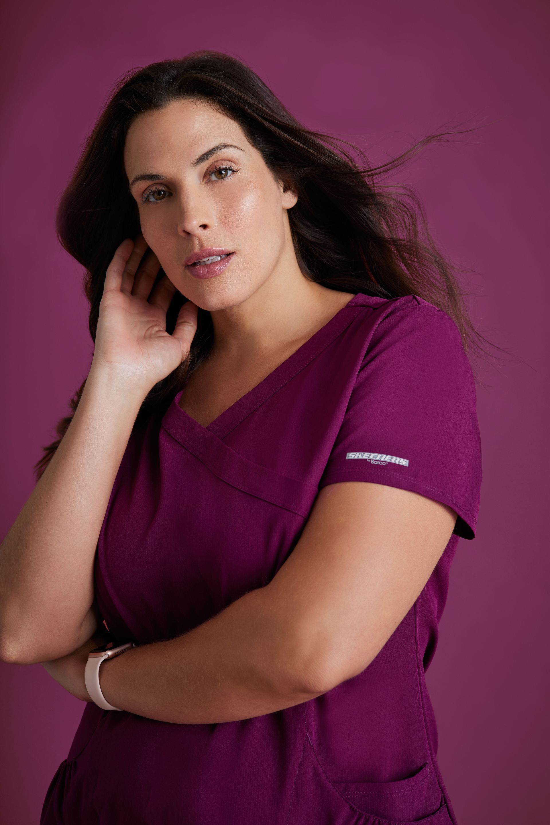 A woman in a purple scrub top is standing in front of a purple background.