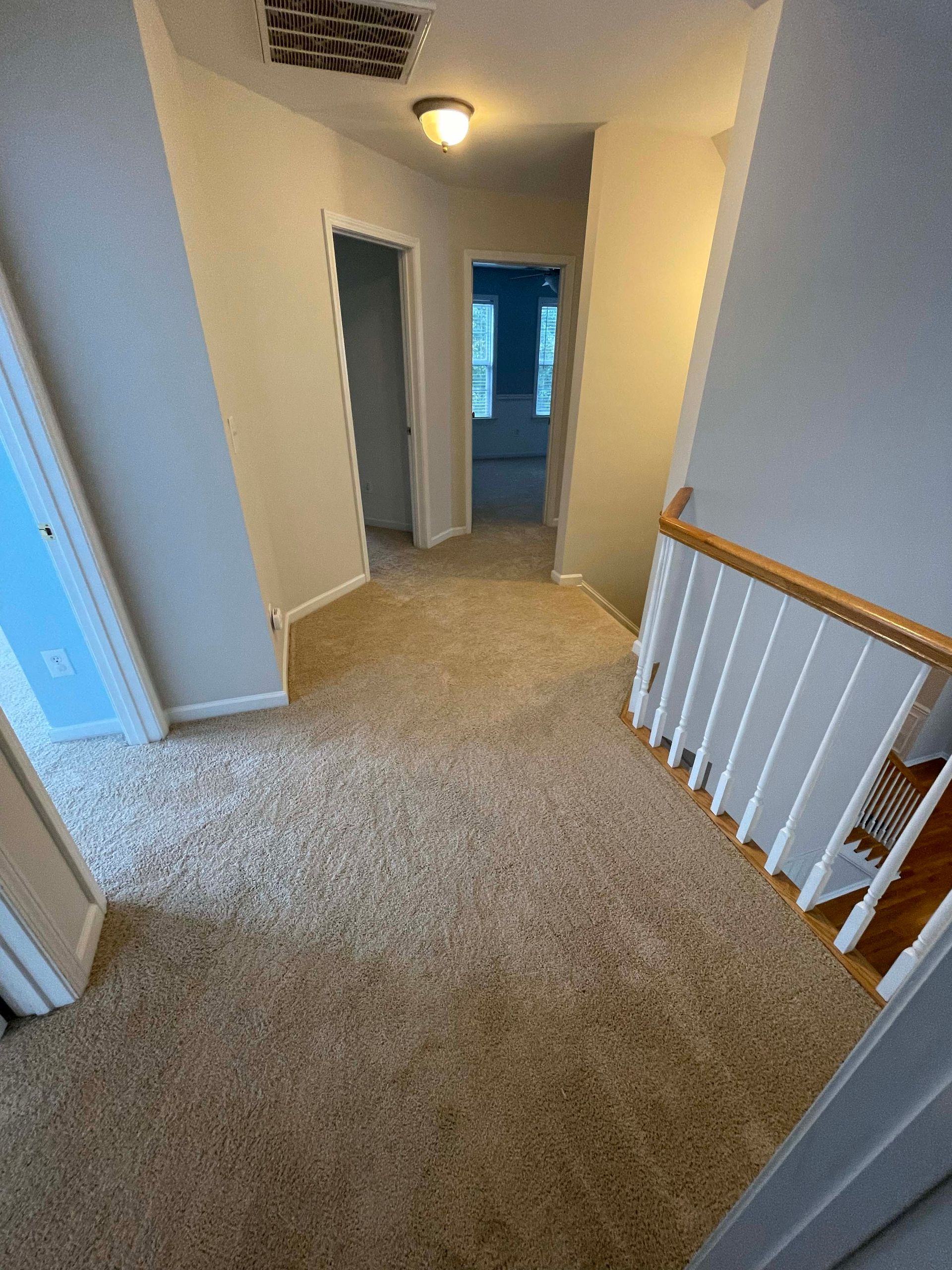 Hallway with beige carpet, doors on either side, and stairs on the right.