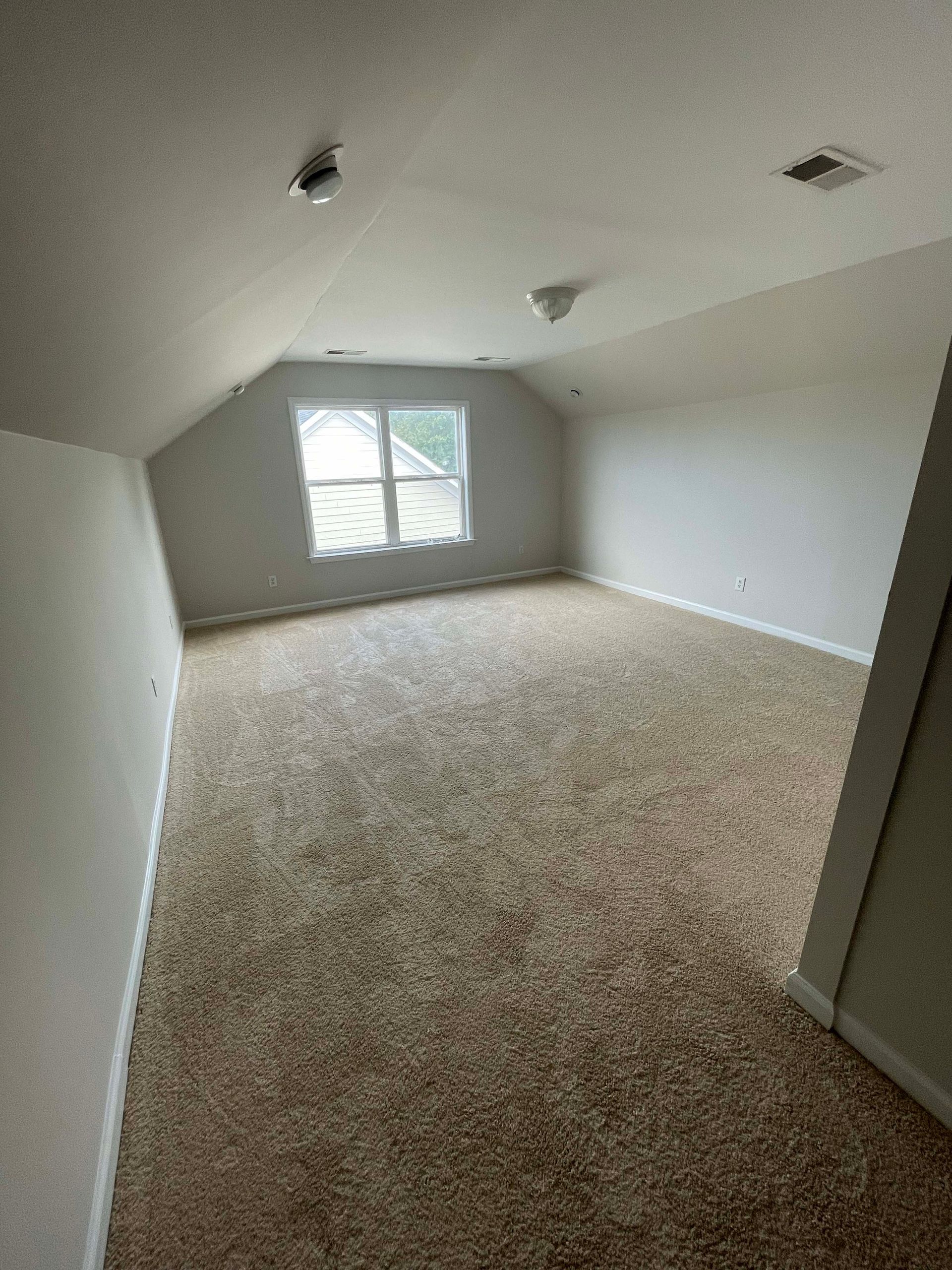 Empty attic room with carpet, small window, slanted walls, and recessed lighting.