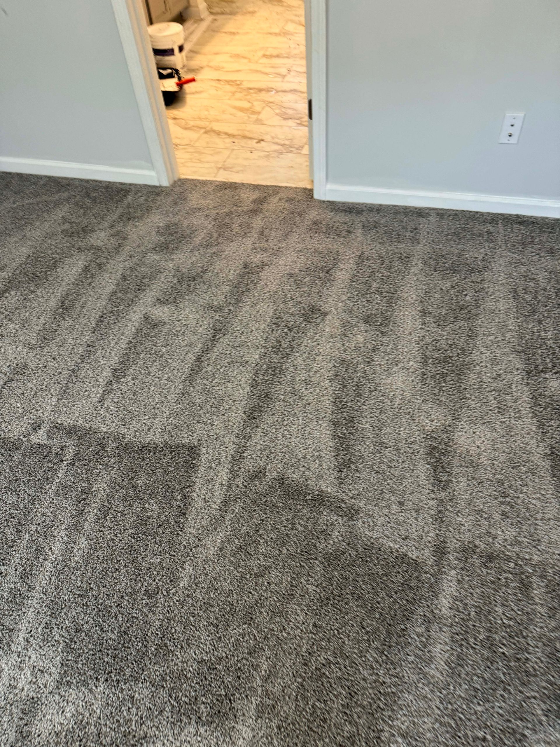 Gray carpeted room leading to a hallway with a light-colored floor; white door trim and light gray walls.