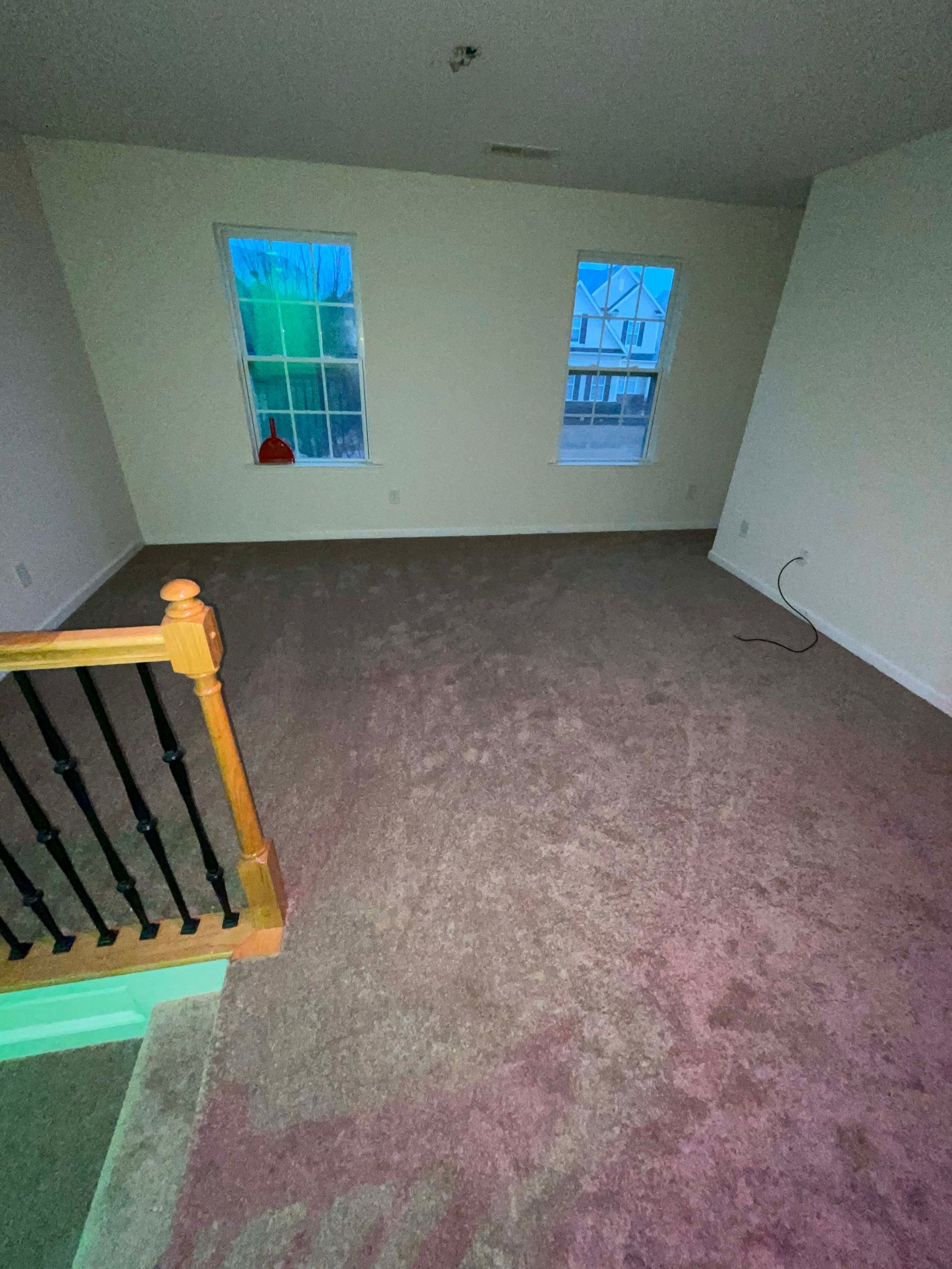 Empty room with brown carpet, two windows with blue light, and a wooden railing.