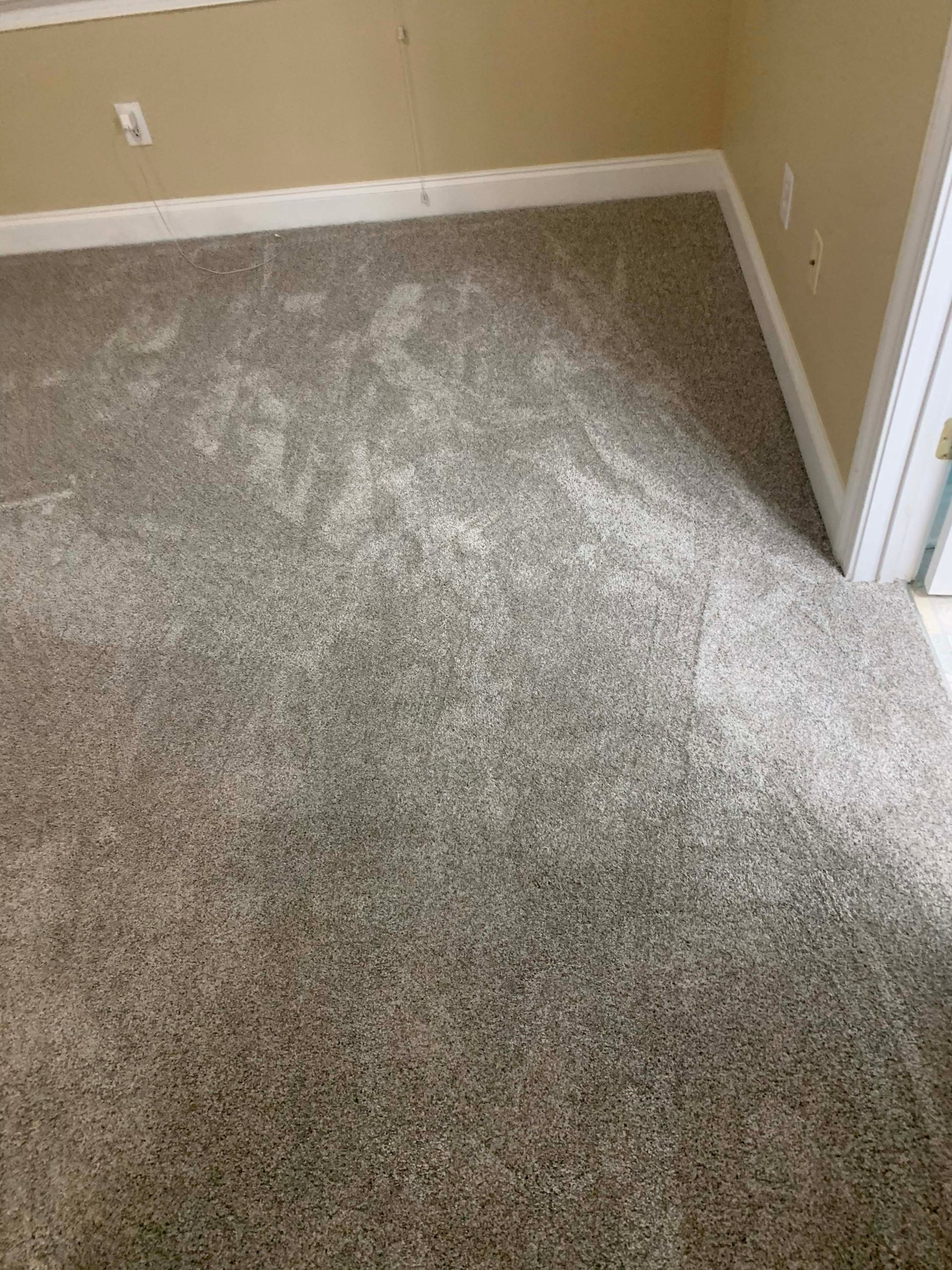 Gray speckled carpeted floor in a room, with white baseboards and wall trim.