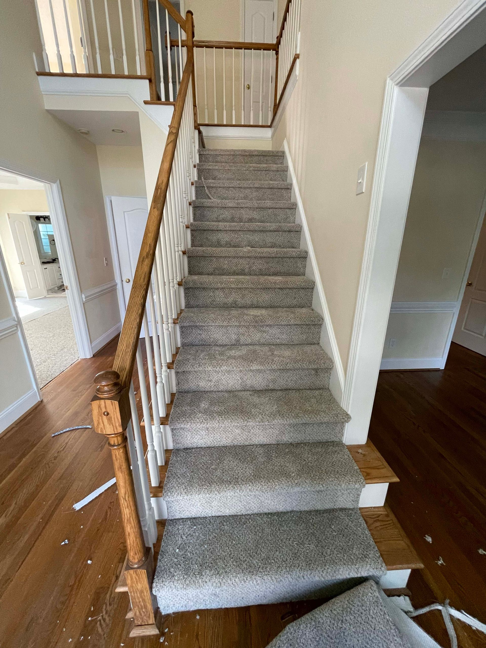 Staircase with carpet and wooden railing. Entryway with hardwood floors and beige walls.