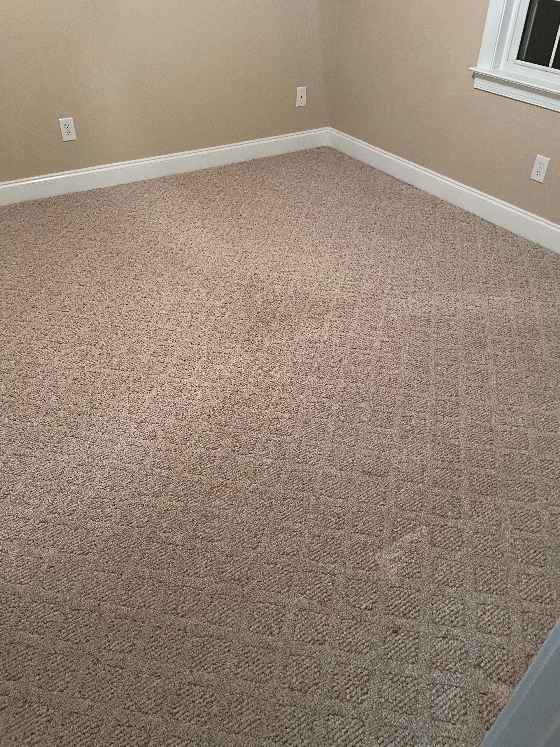 Beige carpet in a room with white trim, beige walls, and electrical outlets.