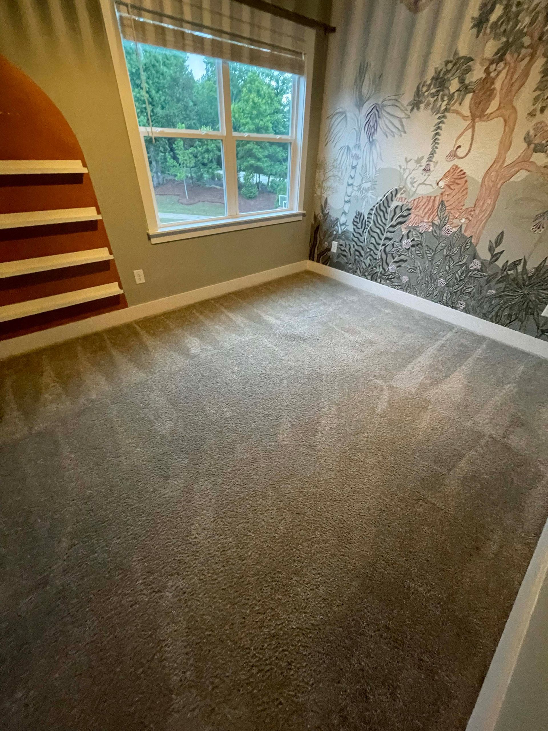 Empty room with gray carpet, a window, and a wall mural of animals and trees.