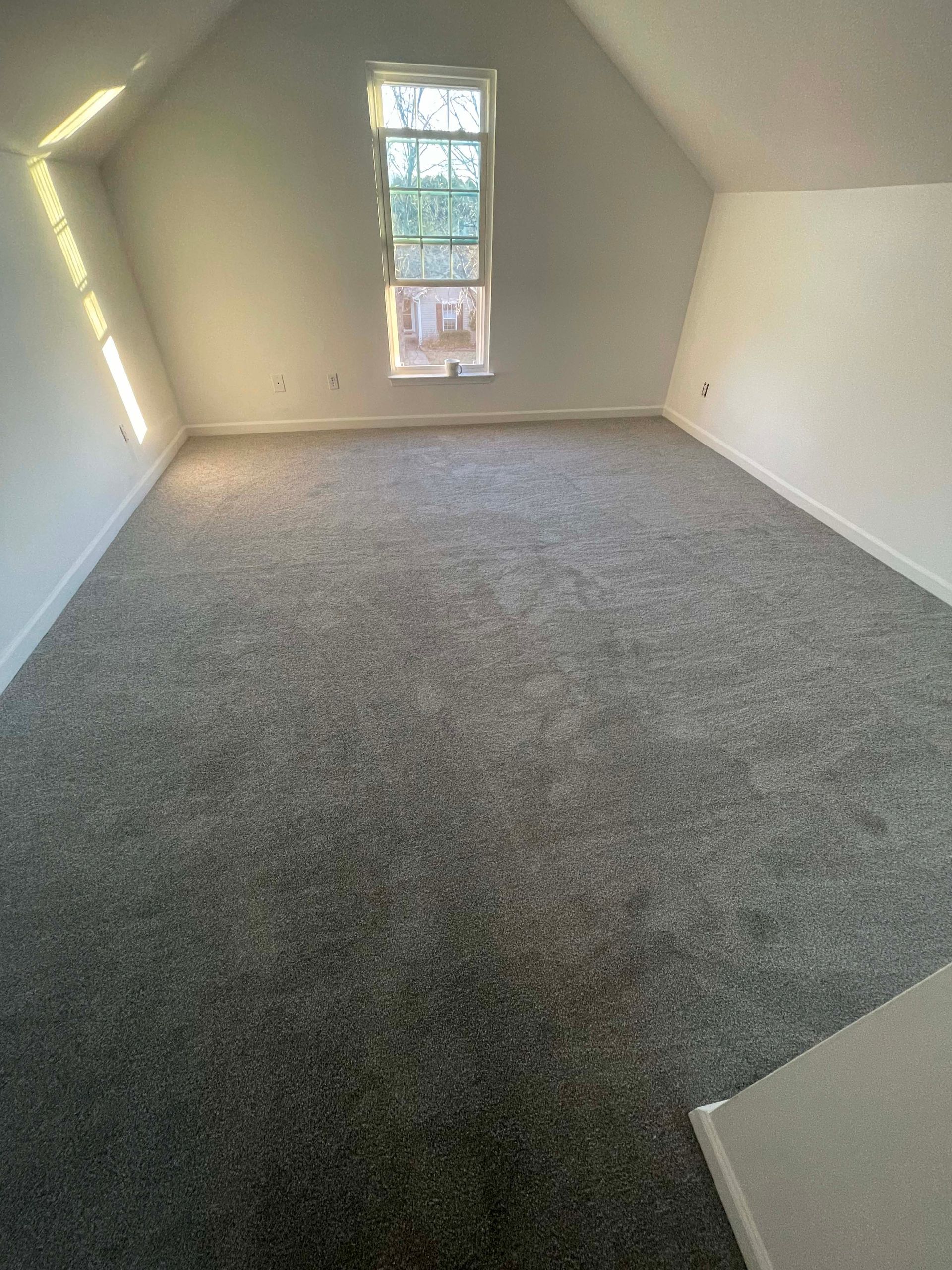 Empty room with gray carpet, a small window, and angled white walls.