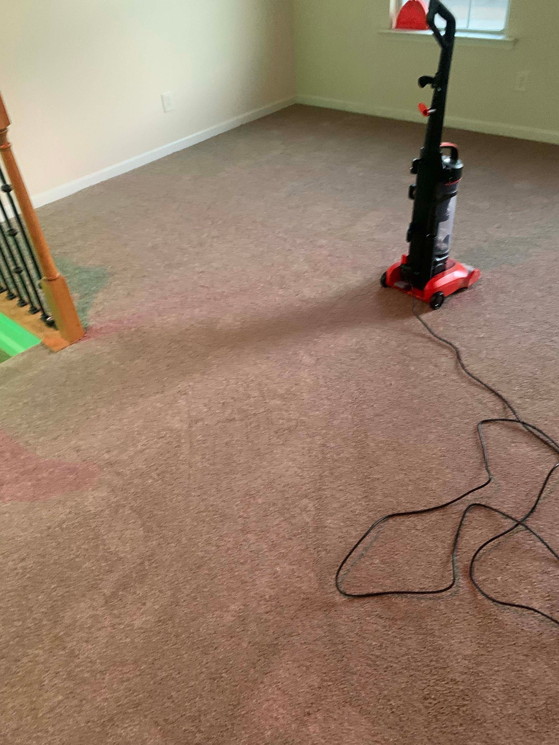 Vacuum cleaner on brown carpet in a room, cord stretched out. Stairs on the left with green paint.