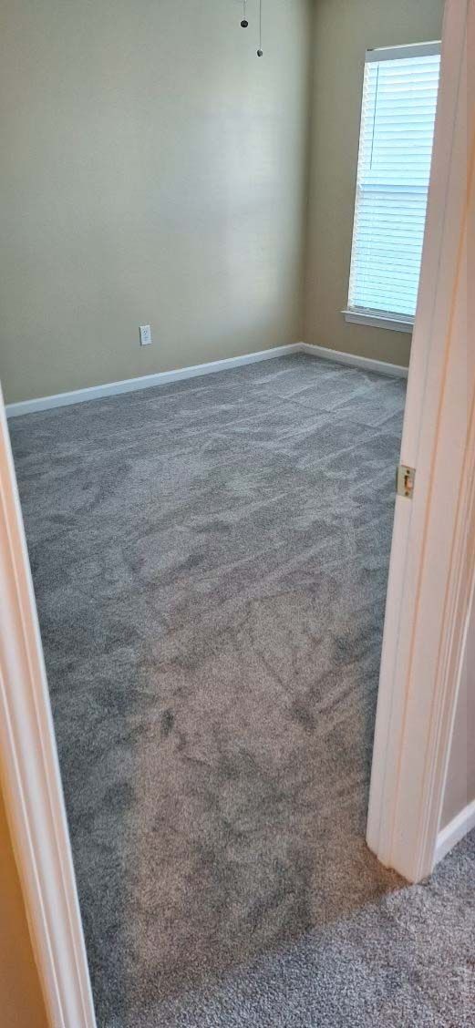 Empty bedroom with gray carpet, tan walls, and a window with blinds.