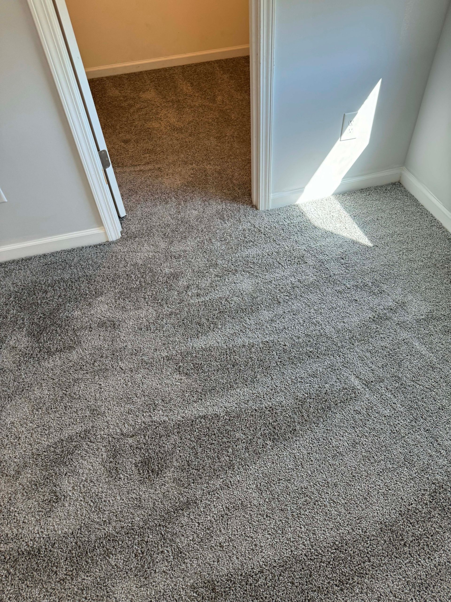 Two rooms with carpet flooring. One with gray carpet, the other with brown carpet. Light on the wall.