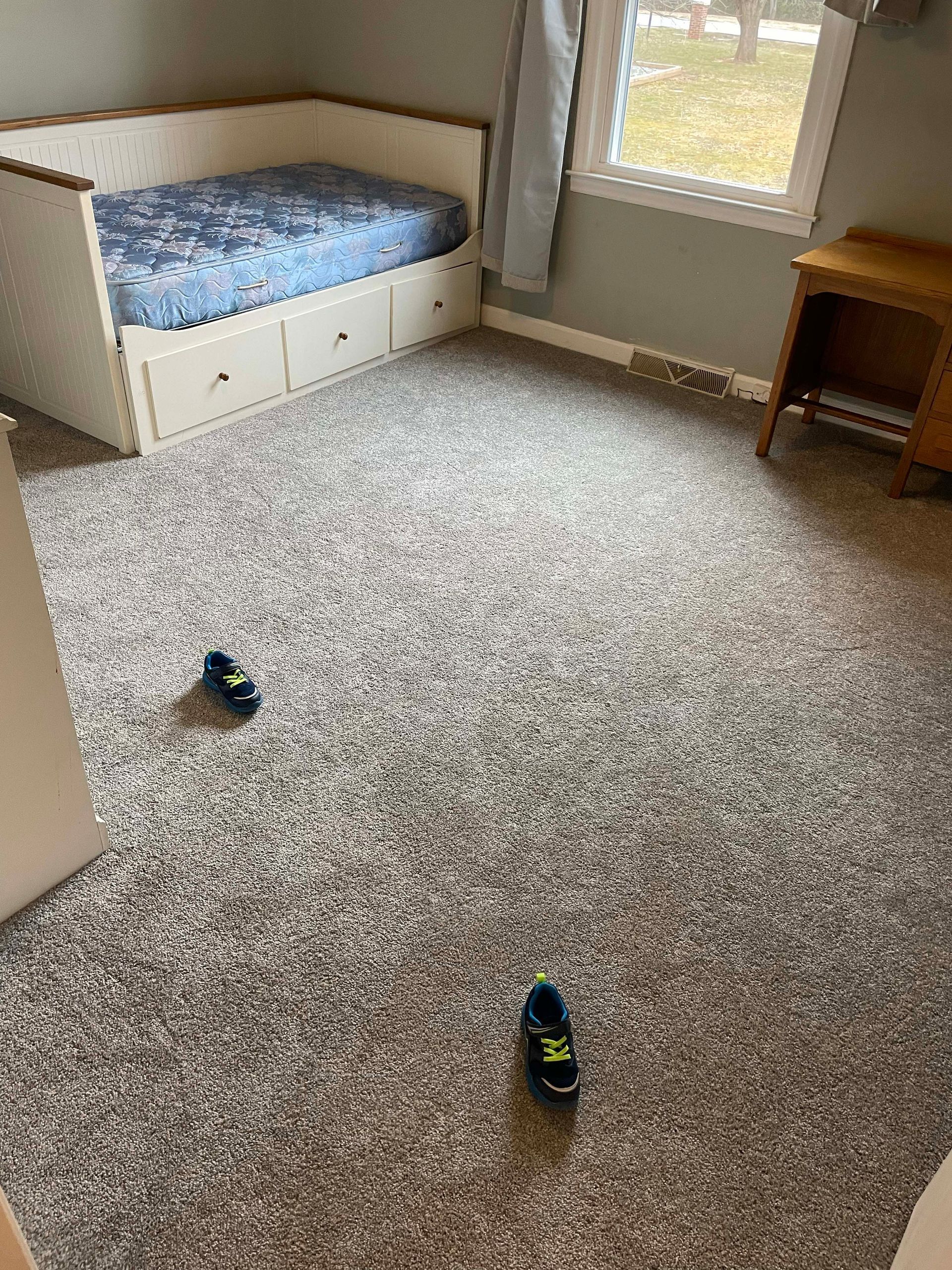 Bedroom with bed, drawers, carpet, small desk, window, and two shoes on the floor.