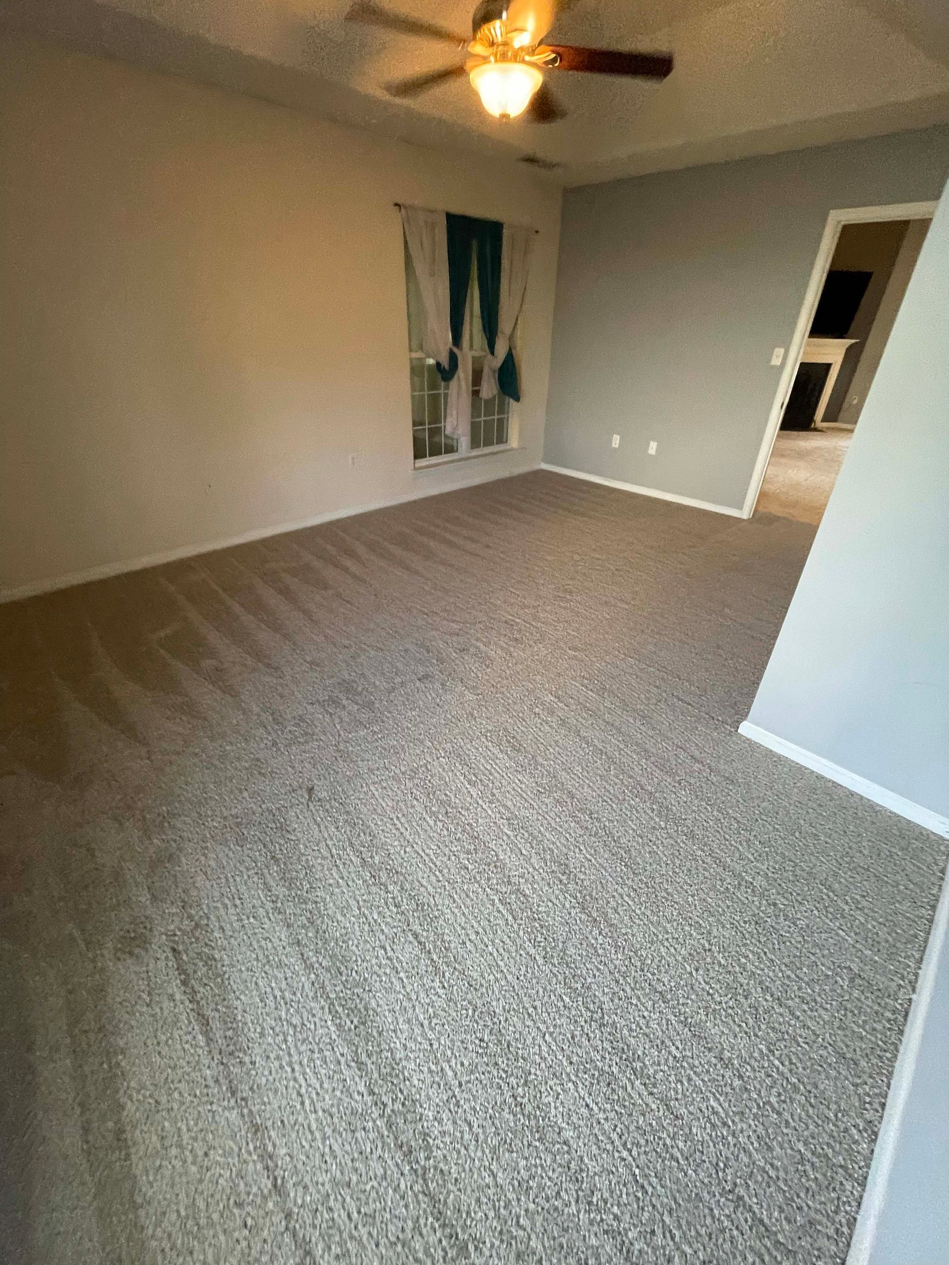 Empty room with gray carpet, light walls, and a window with green curtains.